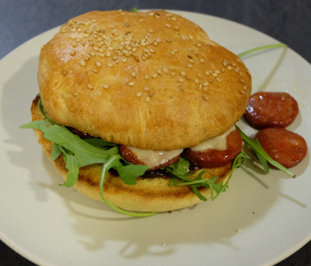 A bun with red onion chutney, fried choriso, rocket and cheddar